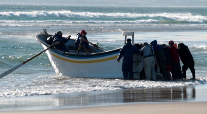 Barco a ser empurrado até quebrar a onde. Para deslizar facilmente a embarcação é rasa em baixo